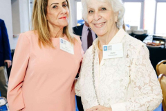 Two women smiling and chatting at a social event in a bright, elegant venue.