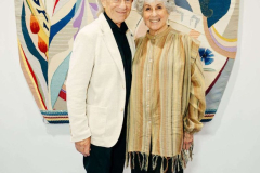 Two women smiling and posing in front of a vibrant, artistic mural at an indoor event.