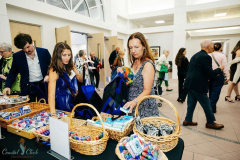 People shopping at a craft fair, browsing handmade accessories and crafts displayed on tables in a bright indoor space.