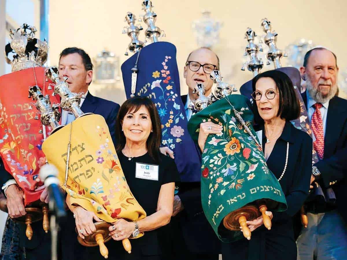 Group of people holding colorful Hanukkah menorahs during celebration.